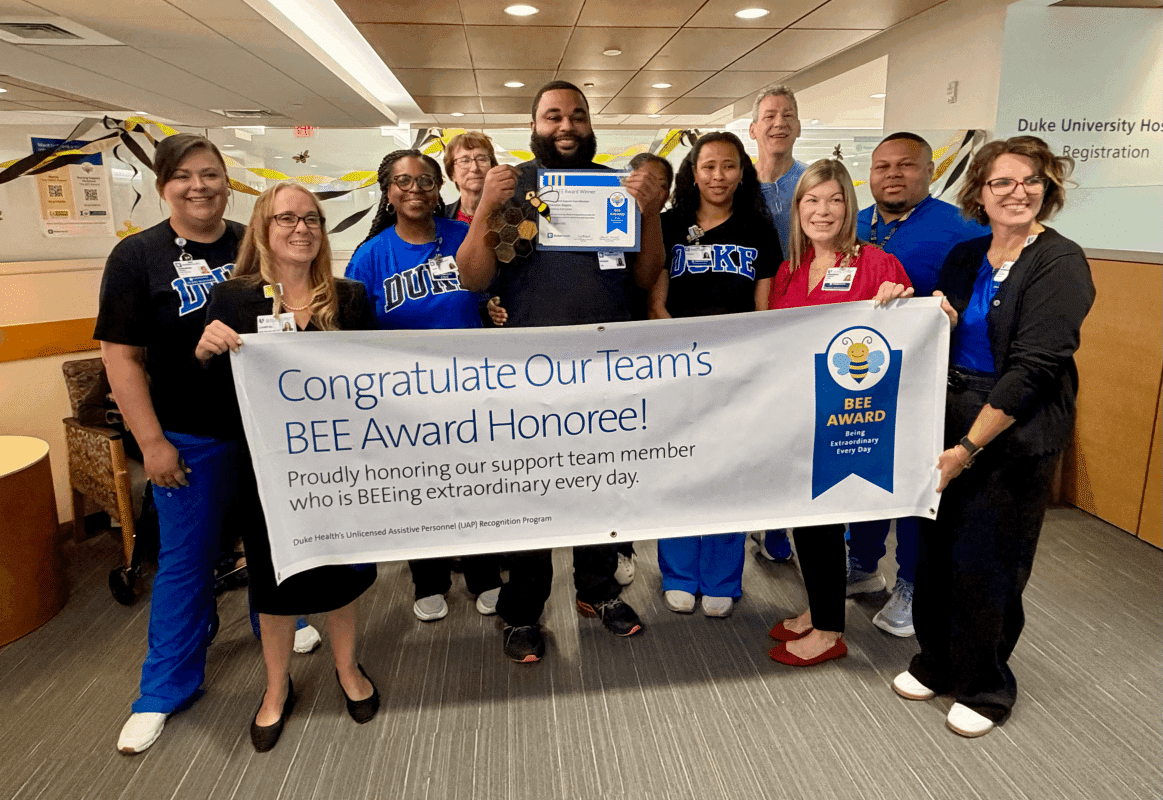 Brandon posing in front of Bee award banner with his co workers 